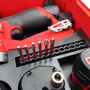May include: A red and black cordless drill and tool set. The set includes a drill, various drill bits, and other tools, all neatly organized within a red case. The drill bits are red and silver.