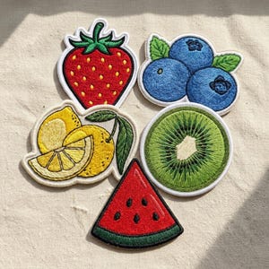 May include: A collection of five embroidered fruit patches featuring a red strawberry, a cluster of blue blueberries with green leaves, a yellow lemon with a leaf, a green kiwi slice, and a red watermelon wedge with black seeds and a green rind.