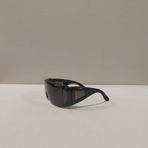 Puede incluir: Gafas de seguridad negras con dise&ntilde;o envolvente. Las gafas tienen lentes oscuras y una montura robusta con ranuras laterales para mayor protecci&oacute;n. Las patillas se curvan para un ajuste seguro. Estas gafas est&aacute;n dise&ntilde;adas para la protecci&oacute;n ocular en diversos entornos laborales.