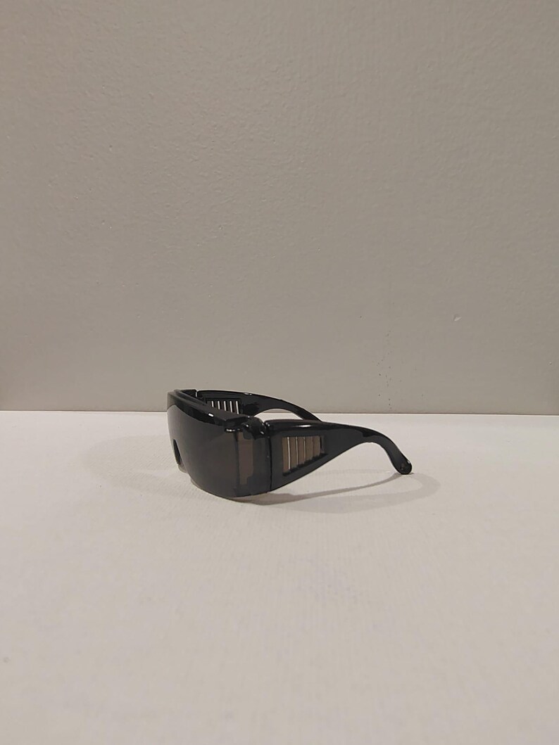 Puede incluir: Gafas de seguridad negras con dise&ntilde;o envolvente. Las gafas tienen lentes oscuras y una montura robusta con ranuras laterales para mayor protecci&oacute;n. Las patillas se curvan para un ajuste seguro. Estas gafas est&aacute;n dise&ntilde;adas para la protecci&oacute;n ocular en diversos entornos laborales.