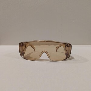 Puede incluir: Gafas de seguridad marrones con dise&ntilde;o envolvente. Las gafas tienen una lente clara y tintada y monturas gruesas y resistentes. Las patillas de las gafas est&aacute;n unidas a la monturas con bisagras. Dise&ntilde;adas para proteger los ojos.