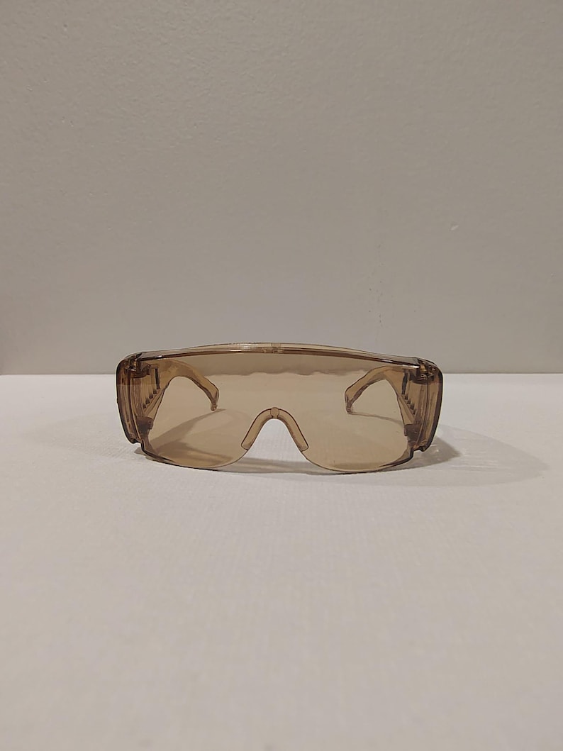 Puede incluir: Gafas de seguridad marrones con dise&ntilde;o envolvente. Las gafas tienen una lente clara y tintada y monturas gruesas y resistentes. Las patillas de las gafas est&aacute;n unidas a la monturas con bisagras. Dise&ntilde;adas para proteger los ojos.