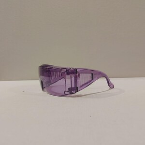 Puede incluir: Un par de gafas de seguridad moradas transparentes. Las gafas tienen un dise&ntilde;o envolvente con una patilla curva para un ajuste seguro. Las lentes y la montura son de color morado s&oacute;lido y transl&uacute;cido, ofreciendo protecci&oacute;n ocular.