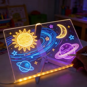 May include: A light-up drawing board with a space theme. The board features a sun, moon, stars, and planets in neon colors. The board is supported by a white stand and is being drawn on with a white marker.