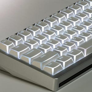 May include: A silver mechanical keyboard with white backlit keys. The keyboard has a compact layout with visible keys including Esc, Tab, CapsLock, Shift, Ctrl, Win, and Alt. The keys are illuminated, creating a bright contrast against the silver frame.