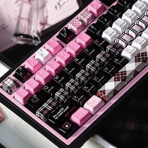 May include: A mechanical keyboard featuring a mix of black, white, and pink keycaps. Some keys display a plaid pattern, while others are solid colors or feature text including "first love" and "You could be my entire world." with a star icon.