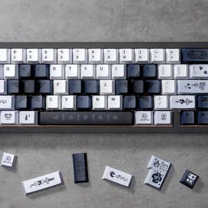 May include: A custom mechanical keyboard with a dark grey frame and a variety of keycaps. The keycaps are white, grey, and black with unique designs and text. Additional keycaps are scattered below the keyboard.
