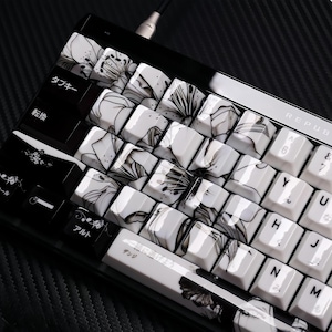 Pode incluir: Um teclado mecânico preto e branco com teclas personalizadas. As teclas apresentam um design floral em tons de cinza e branco. O teclado tem caracteres japoneses em algumas teclas.