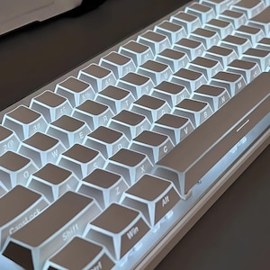 May include: A white mechanical keyboard with illuminated keys. The keyboard has a compact layout with various function keys and alphanumeric keys. The keycaps are white with black lettering. The keyboard is designed for gaming or typing.