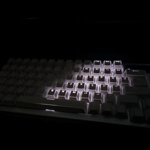 Op de afbeelding: Een mechanisch toetsenbord met verlichte witte toetsen. De toetsen zijn wit en de achtergrondverlichting zorgt voor een heldere gloed tegen de donkere achtergrond. Dit toetsenbord is ontworpen voor gaming of professioneel gebruik.