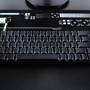 May include: A black mechanical keyboard with square keycaps. The keyboard has a compact layout and a coiled white cable. The background is black with white graphic elements. The keyboard is designed for gaming or typing.