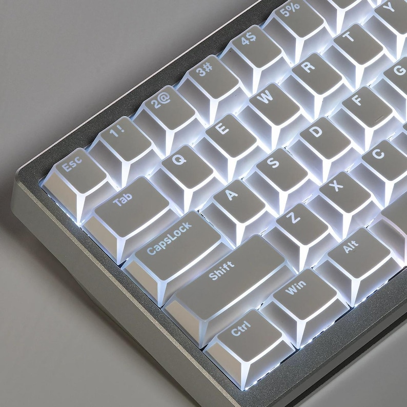 Op de afbeelding: Close-up van een mechanisch toetsenbord met witte keycaps en een zilveren frame. De toetsen zijn verlicht met een helder wit licht. De toetsenbordindeling bevat standaardtoetsen zoals Tab, CapsLock, Shift, Ctrl en Alt.