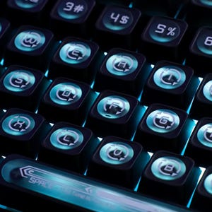 May include: Close-up of a black mechanical keyboard with illuminated teal keys. The keys feature white symbols and letters, with the space bar displaying the text "SPACE Time is". The keyboard has a futuristic design.
