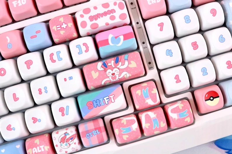 May include: A close-up of a keyboard with custom keycaps in pink, white, and blue. The keycaps feature various designs, including hearts, cartoon characters, and the word "SHIFT". Numbers and letters are also visible.
