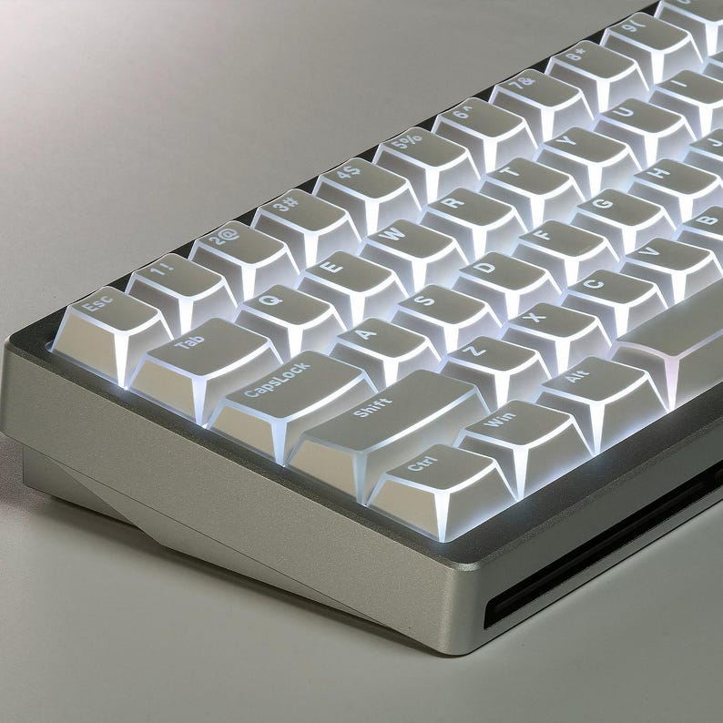 Op de afbeelding: Een zilverkleurig mechanisch toetsenbord met wit verlichte toetsen. Het toetsenbord heeft een compacte lay-out met zichtbare toetsen zoals Esc, Tab, CapsLock, Shift, Ctrl, Win en Alt. De toetsen zijn verlicht, wat een helder contrast cre&euml;ert.