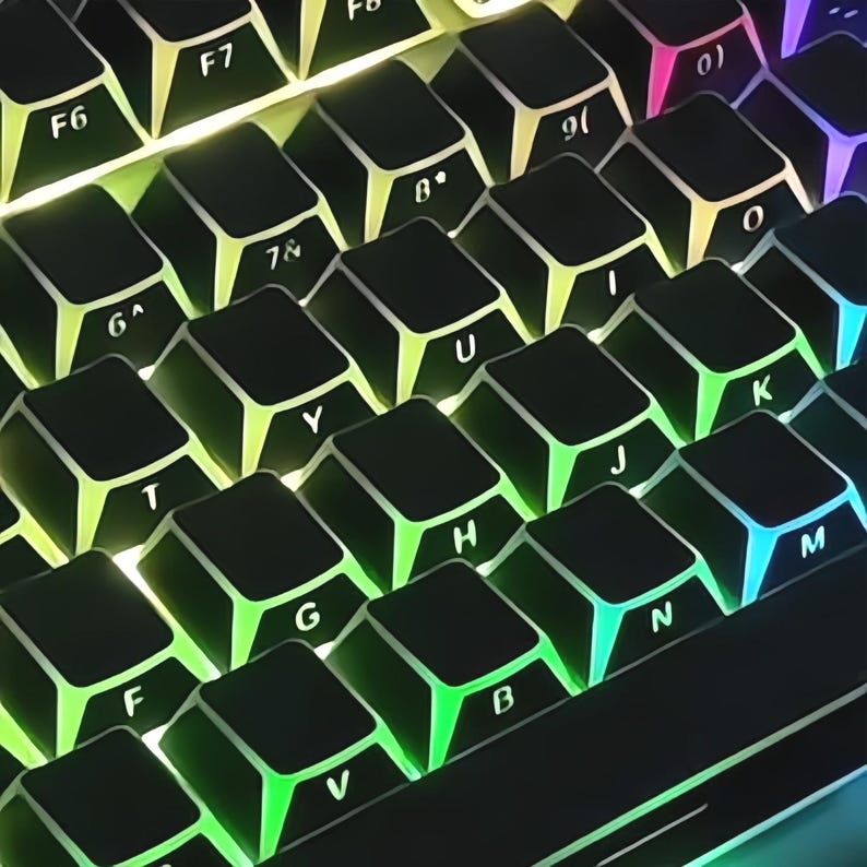 May include: Close-up of a black mechanical keyboard with illuminated keys. The keys are black with white lettering and feature a rainbow of LED backlighting. The keyboard layout includes function keys, numbers, and letters.