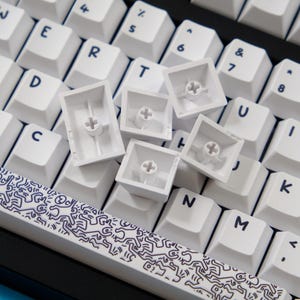 May include: Close-up of a white mechanical keyboard with keycaps removed. The keyboard has white keycaps with black lettering. A spacebar with a black and white graphic design is visible.