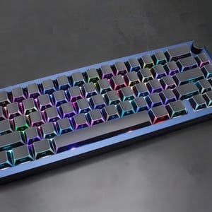 May include: A blue mechanical keyboard with backlit keys. The keyboard has a dark frame and a volume control knob. The keys are black with multi-coloured backlighting, creating a vibrant display. The keyboard is designed for gaming or professional use.
