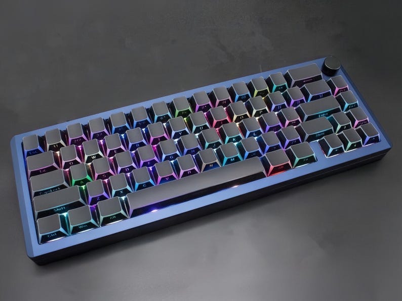 May include: A blue mechanical keyboard with backlit keys. The keyboard has a dark frame and a volume control knob. The keys are black with multi-coloured backlighting, creating a vibrant display. The keyboard is designed for gaming or professional use.