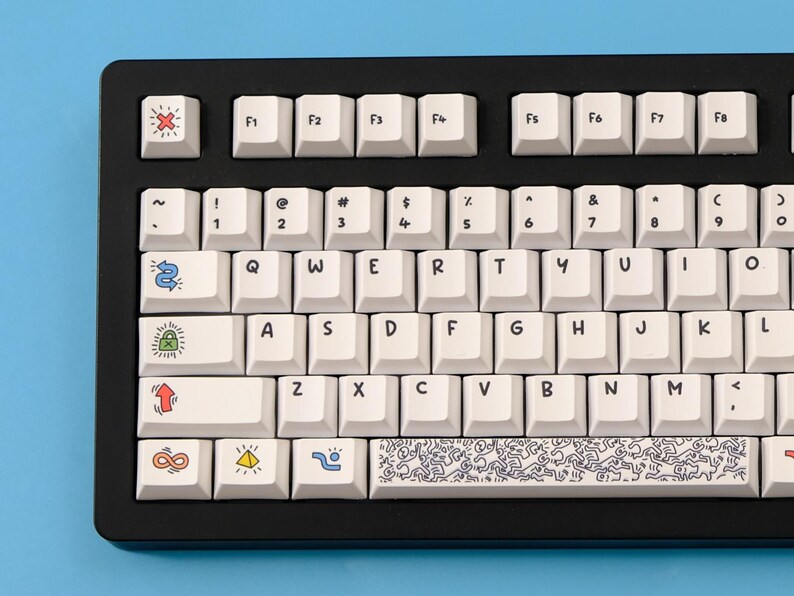 May include: Black mechanical keyboard with white keycaps. Some keycaps feature colorful cartoon graphics and symbols. The keyboard has a standard QWERTY layout with function keys.