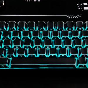 May include: A black mechanical keyboard with teal illuminated keys. The keyboard has a standard QWERTY layout with function keys and a space bar. The keys are backlit, creating a vibrant glow. The keyboard is designed for gaming or typing.