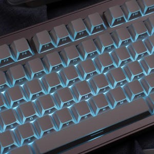 May include: A close-up of a mechanical keyboard with white keycaps and blue backlighting. The keyboard has a standard QWERTY layout with function keys and number keys. The keycaps are evenly spaced and the lighting is bright.