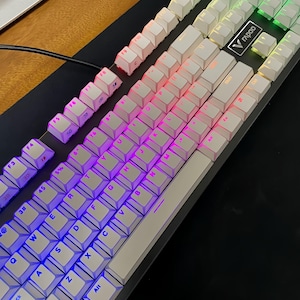 Op de afbeelding: Een witte mechanische toetsenbord met verlichte toetsen. De toetsen zijn verlicht met een kleurengradi&euml;nt van blauw, paars, roze en groen. Het toetsenbord heeft een zwarte basis en een zilveren frame. De merknaam "Rapoo" is zichtbaar.