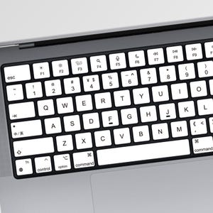 Puede incluir: Un teclado de ordenador portátil con teclas blancas y letras negras sobre un marco gris oscuro. La disposición incluye teclas QWERTY estándar, una fila superior de teclas de función con iconos y teclas de comando, opción y control.