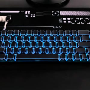May include: A black mechanical keyboard with blue LED backlighting. The keyboard has a compact design with a 60% layout. The keys are black with white lettering. The keyboard is on a black surface with white graphic designs.
