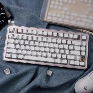 May include: A silver and white mechanical keyboard with a rose gold frame. The keyboard has white keycaps and a few brown accent keys. A white mouse and extra keycaps are also visible.