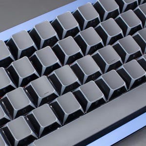May include: Close-up of a mechanical keyboard with grey keycaps and white lettering. The keys are arranged in a grid pattern, with a silver trim around the base of each key. The keyboard has a blue backlight.
