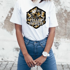 May include: White t-shirt featuring a hexagonal design with a bee graphic and the words "YELLOW JACKETS" in a bold font. The bee is yellow and black, set against a camouflage pattern. The shirt is paired with blue jeans and a white watch.