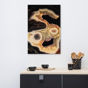 Puede incluir: Una impresión de arte mural rectangular con un diseño abstracto vertical de patrones de piedra ágata en capas en tonos negro, crema y dorado. La composición muestra anillos concéntricos, texturas cristalinas y vacíos negros profundos.