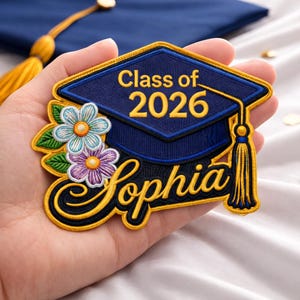 May include: Embroidered patch featuring a graduation cap design with the text "Class of 2026" and the name "Sophia". The patch is navy blue, gold, and features floral accents.