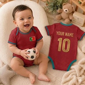 May include: A maroon baby bodysuit with a wavy pattern, teal trim, and the Portugal flag on the chest. A matching bodysuit is displayed next to it, featuring the text YOUR NAME and the number 10 in gold lettering on the back of the garment.