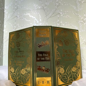 May include: A set of three hardcover books with green covers and gold accents. The titles include "The Cruel Prince," "The Wicked King," "The Queen of Nothing," and "The Folk of the Air." The spine reads "The Folk of the Air" and "I-II-III."