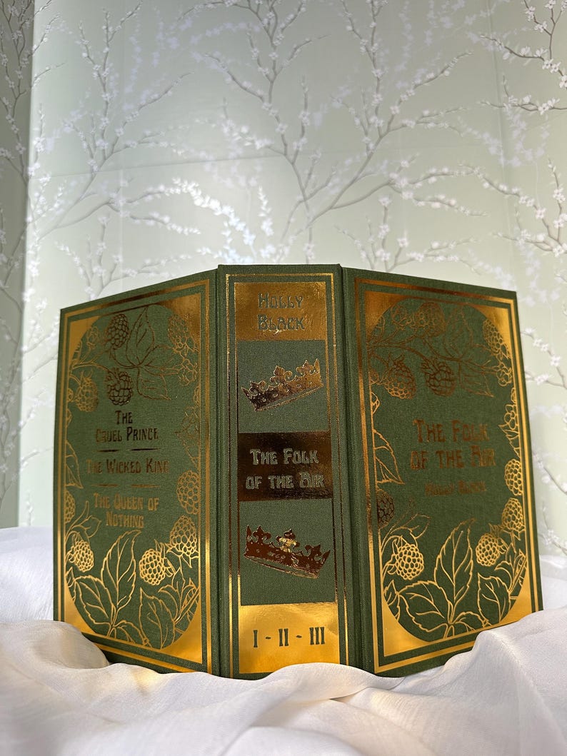 May include: A set of three hardcover books with green covers and gold accents. The titles include "The Cruel Prince," "The Wicked King," "The Queen of Nothing," and "The Folk of the Air." The spine reads "The Folk of the Air" and "I-II-III."