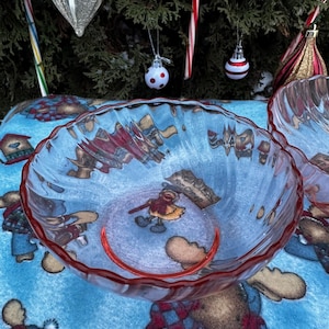 Könnte beinhalten: Klarer Glasnapf mit rotem, gewelltem Rand. Die Schüssel hat ein Wintermotiv mit Zeichentrickfiguren und dem Text "For Cindy". Die Schüssel steht auf einer blau gemusterten Tischdecke mit Weihnachtsdekorationen im Hintergrund.