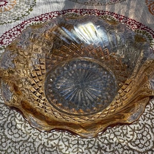 Könnte beinhalten: Eine bernsteinfarbene Glasschale mit Rautenmuster und gewelltem Rand. Die Schale hat einen kreisförmigen Boden mit einem Sternmuster. Das Glas reflektiert das Licht und erzeugt Glanzlichter und Schatten. Die Schale ist wahrscheinlich Vintage oder antik.
