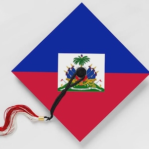 May include: A graduation cap featuring the flag of Haiti. The cap is divided into blue and red sections, with the Haitian coat of arms in the center. A black tassel with red and white accents hangs from the cap.