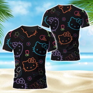 May include: Black t-shirts featuring a repeating pattern of Hello Kitty faces, stars, flowers, and ice cream cones in neon colours. The words "HELLO KITTY" are printed on the bottom. The shirts are displayed against a beach background.