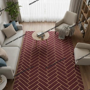 May include: A burgundy and beige herringbone pattern rug in a living room setting. The rug is the focal point, with a sofa, chairs, and a coffee table arranged around it. The room has wooden floors and natural light.
