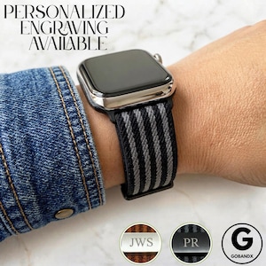 May include: A smartwatch with a metallic silver casing and a black and grey striped elastic fabric band. The text PERSONALIZED ENGRAVING AVAILABLE is visible at the top. Two circular insets show metal tags engraved with JWS and PR.