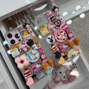 Pu&ograve; includere: Custodia per telefono trasparente decorata con vari ciondoli 3D, tra cui personaggi di Hello Kitty, dessert e la scritta "RICH!". La custodia presenta anche un cinturino da polso tempestato di gioielli, il tutto in un cassetto bianco.