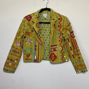 May include: A chartreuse blazer with colourful embroidered details and embellishments. The jacket features a notched collar, long sleeves, and a button closure. The embroidery includes floral and geometric patterns in red, blue, and orange.