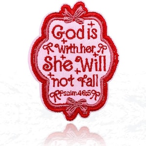 May include: Embroidered patch with the text "God is with her, She Will not Fall" in red thread on a pink background. The patch has a decorative red border with bow accents and the scripture reference Psalm 46:5.