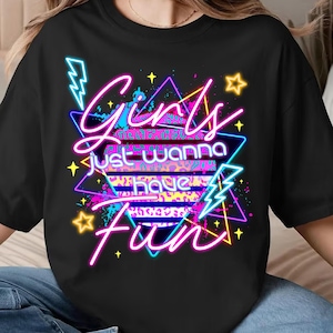 May include: Black t-shirt with a neon graphic that reads "Girls just wanna have fun." The design features pink, blue, and yellow text, lightning bolts, stars, and a leopard print background.