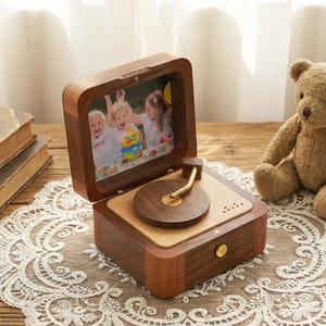 May include: A wooden music box with a photo frame lid, featuring a picture of three children. The box has a turntable design with a wooden record and a gold-colored tone arm. A small gold knob is on the front.