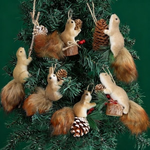 May include: A collection of squirrel ornaments hanging on a green Christmas tree. The ornaments are light brown with fluffy, reddish-brown tails. Some squirrels hold pinecones or sit on small wooden platforms. Red berries add a festive touch.
