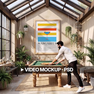 May include: A framed "Margarita" cocktail recipe poster with colorful horizontal stripes hangs above a pool table. The room features hanging plants, a large window, and a man setting a pizza on the table. The text "VIDEO MOCKUP • PSD" is at the bottom.